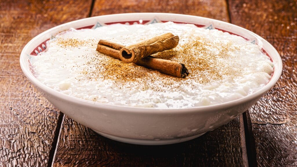 Uma porção de arroz doce com textura cremosa, grãos de arroz envolvidos por um creme suave e finalizada com canela.